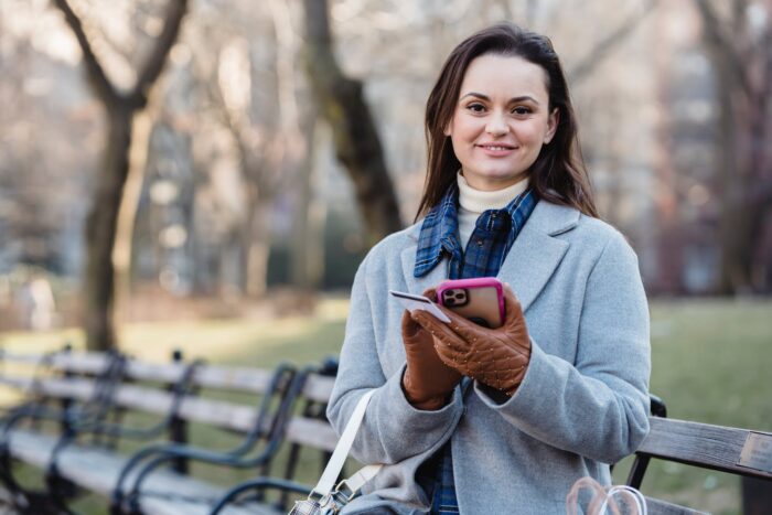 smiling woman using smartphone on spring city park
